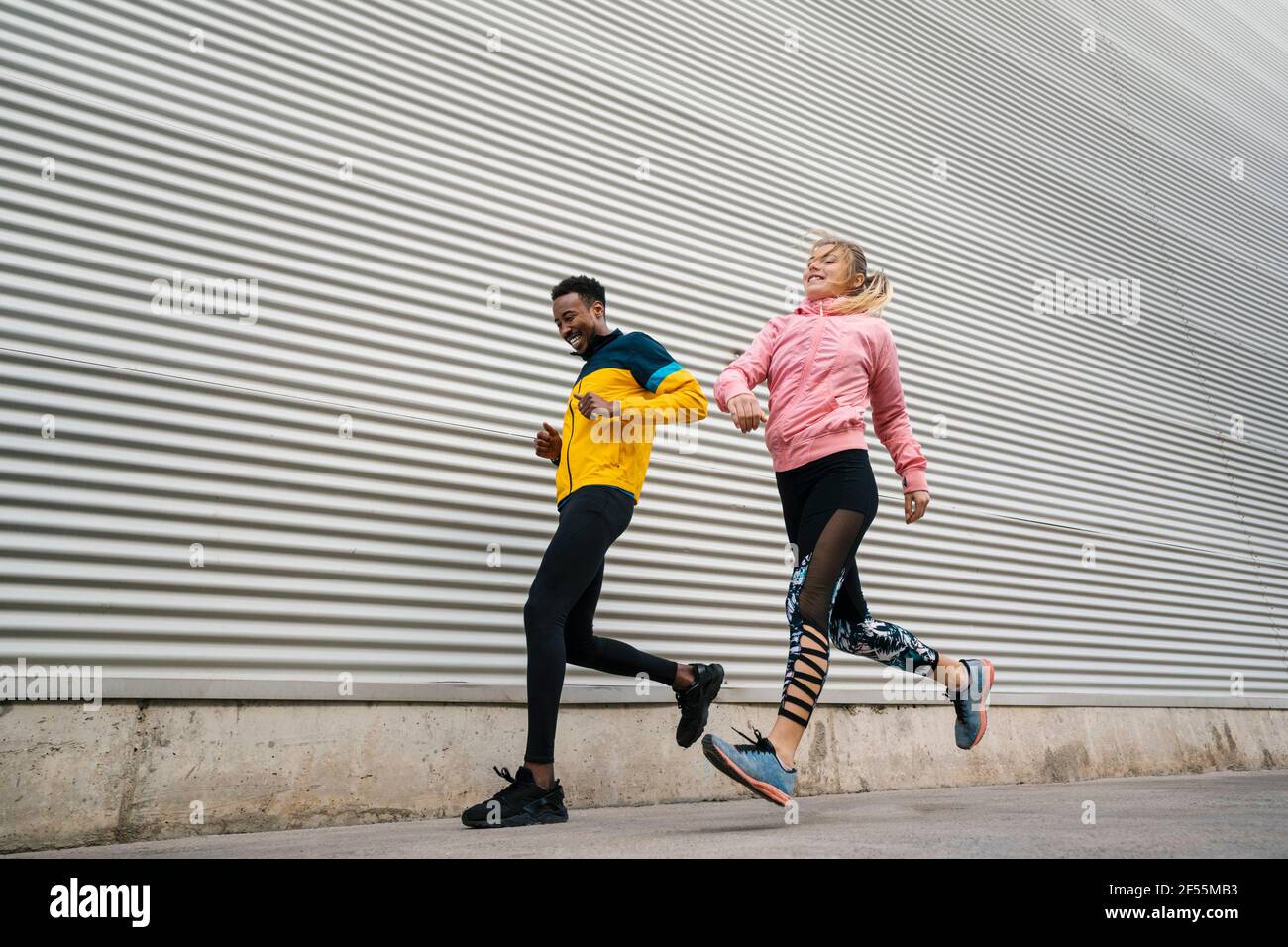 Cheerful male and female friends running by wall Stock Photo