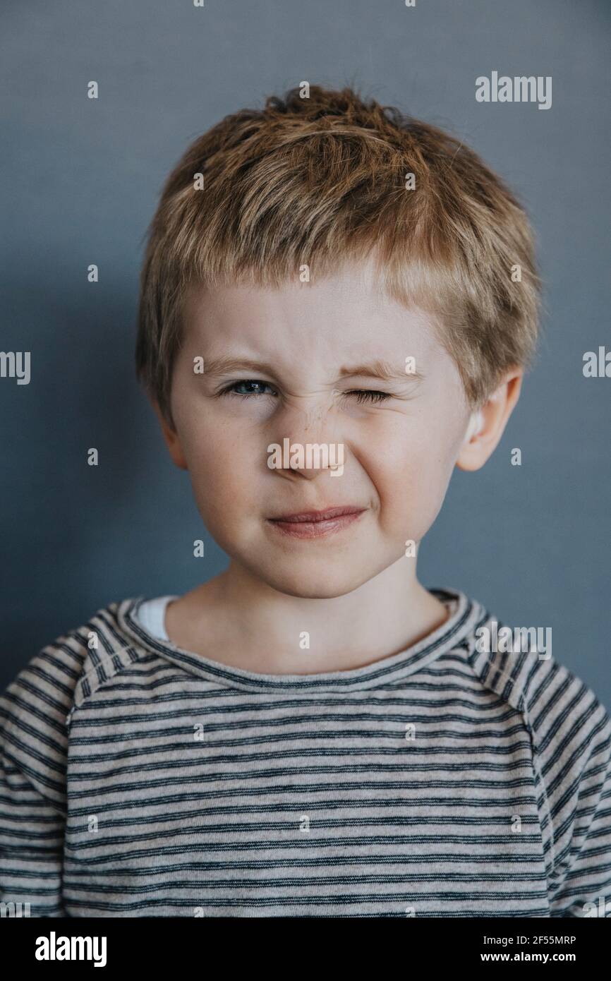 Playful boy winking against gray background Stock Photo