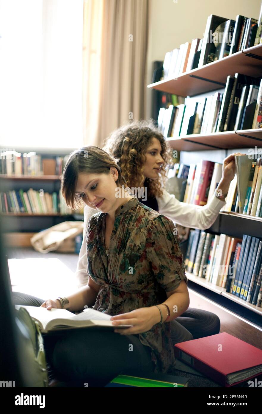 Female students reading books while sitting in library Stock Photo