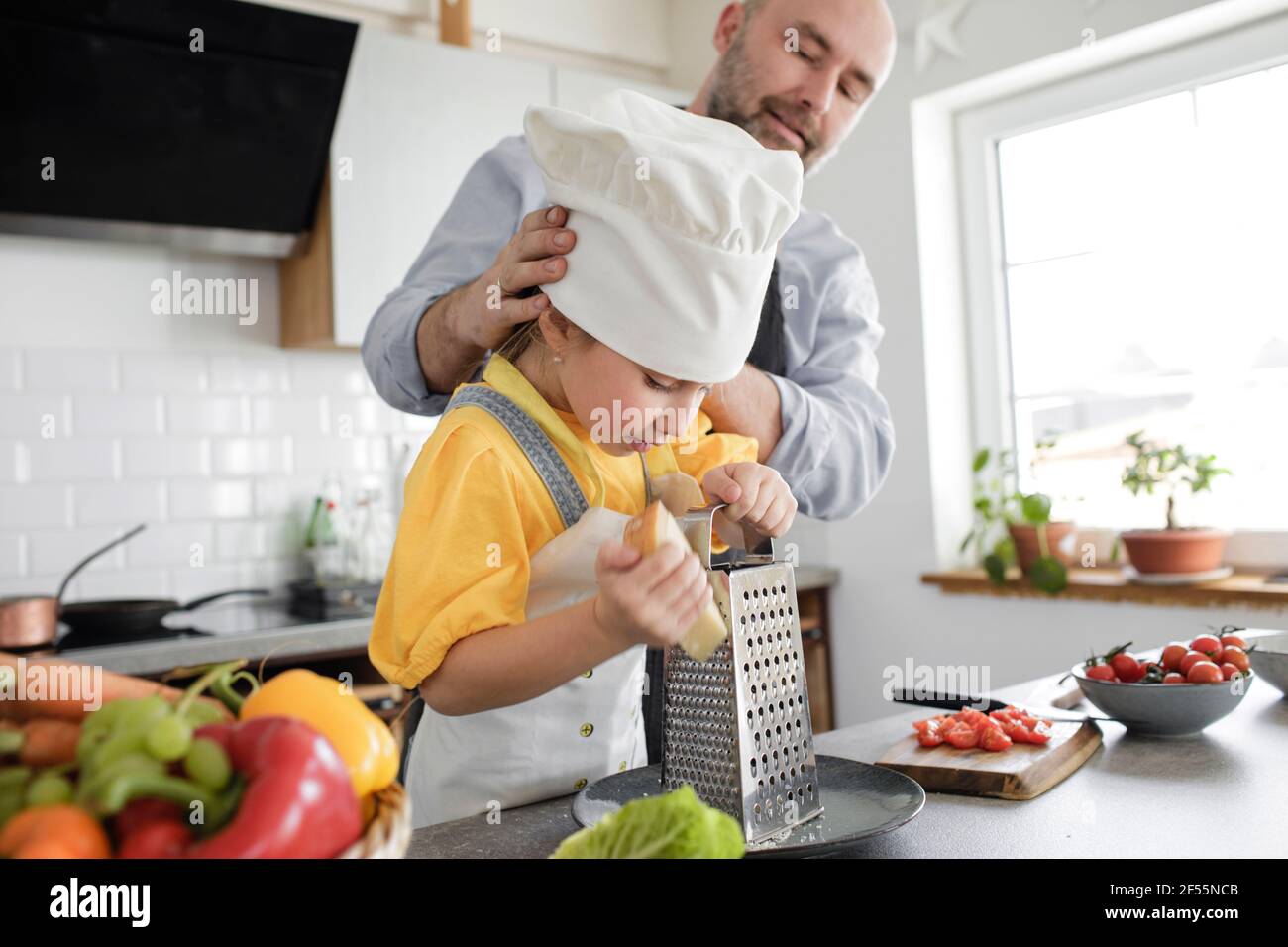 Mature men adjusting girl chef's hat while standing at kitchen Stock Photo