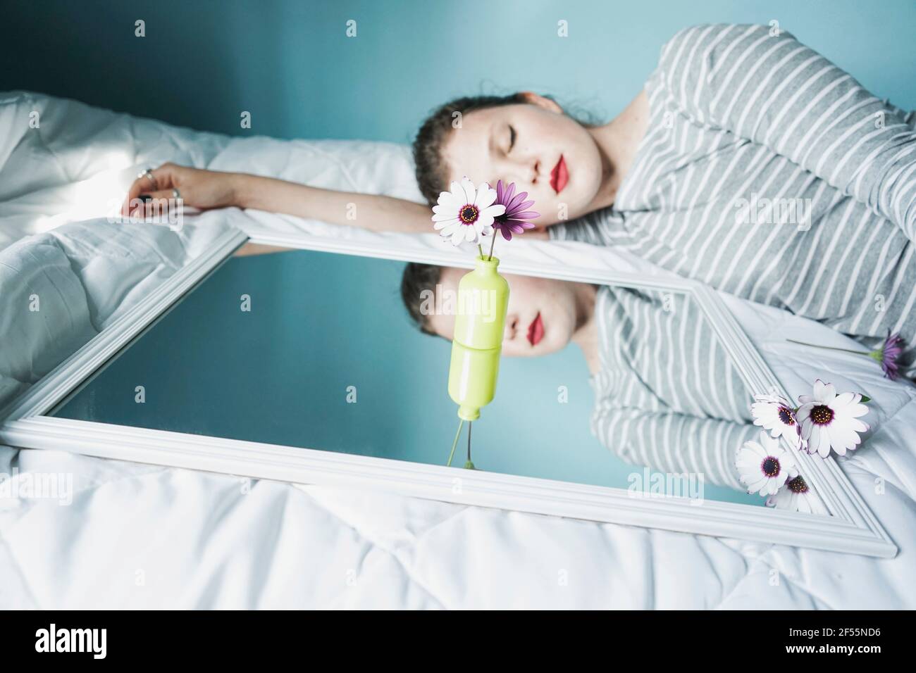 Young woman sleeping next to mirror lying on white duvet Stock Photo