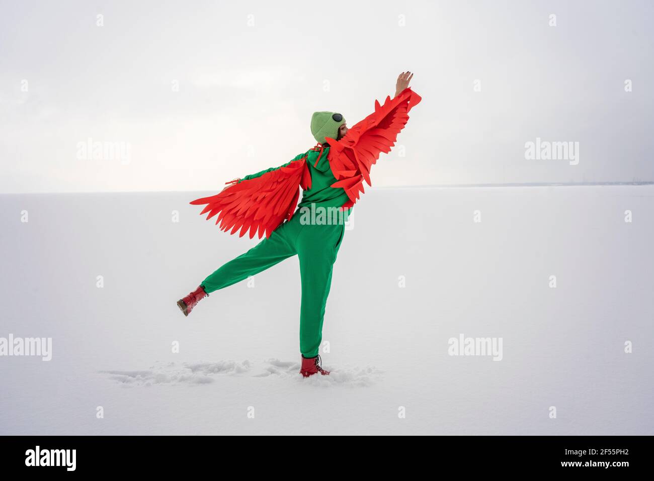 Woman with wings flying on snow while wearing bird's costume Stock Photo