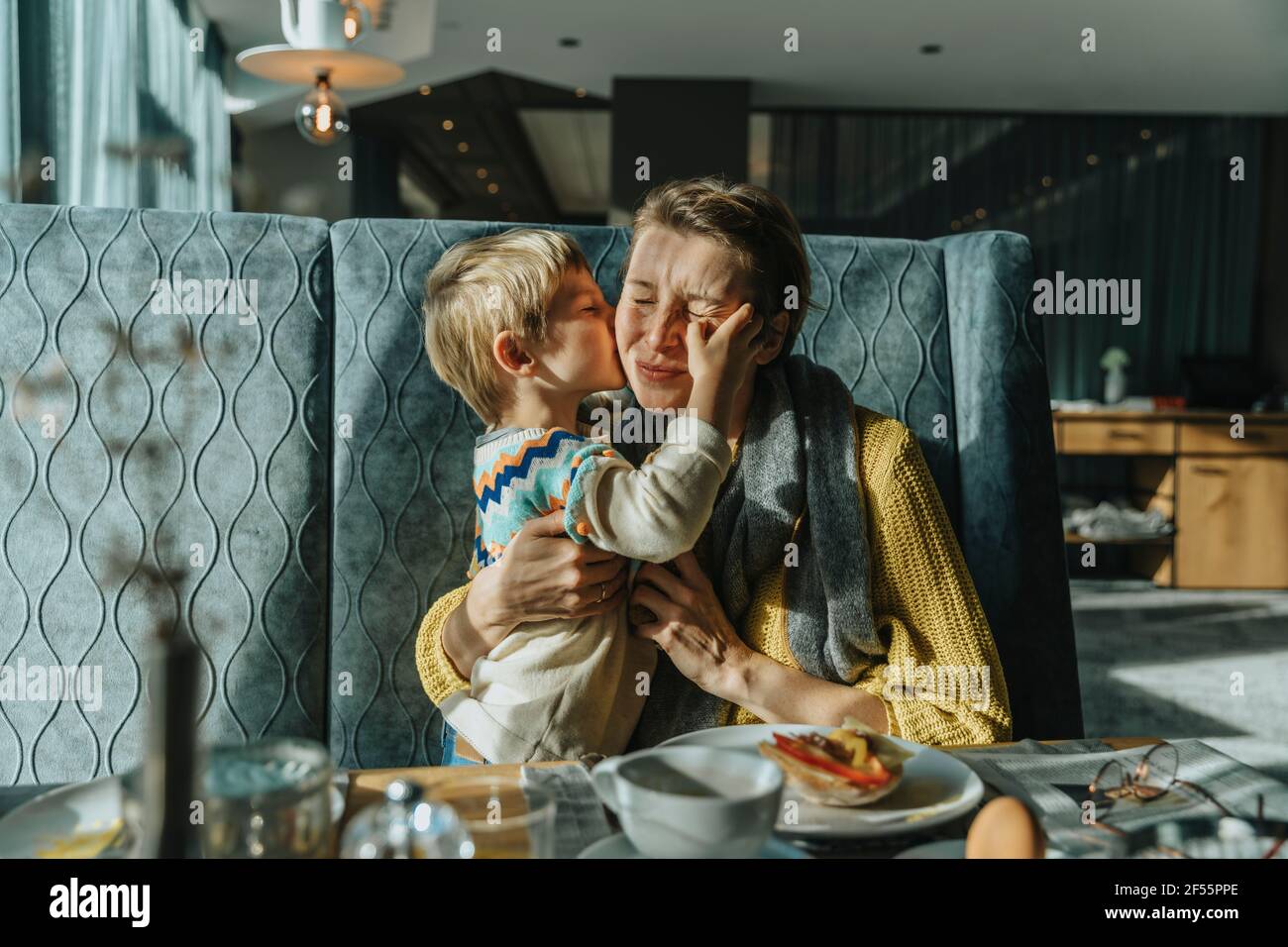 Son kissing mother while sitting at table in hotel room Stock Photo - Alamy