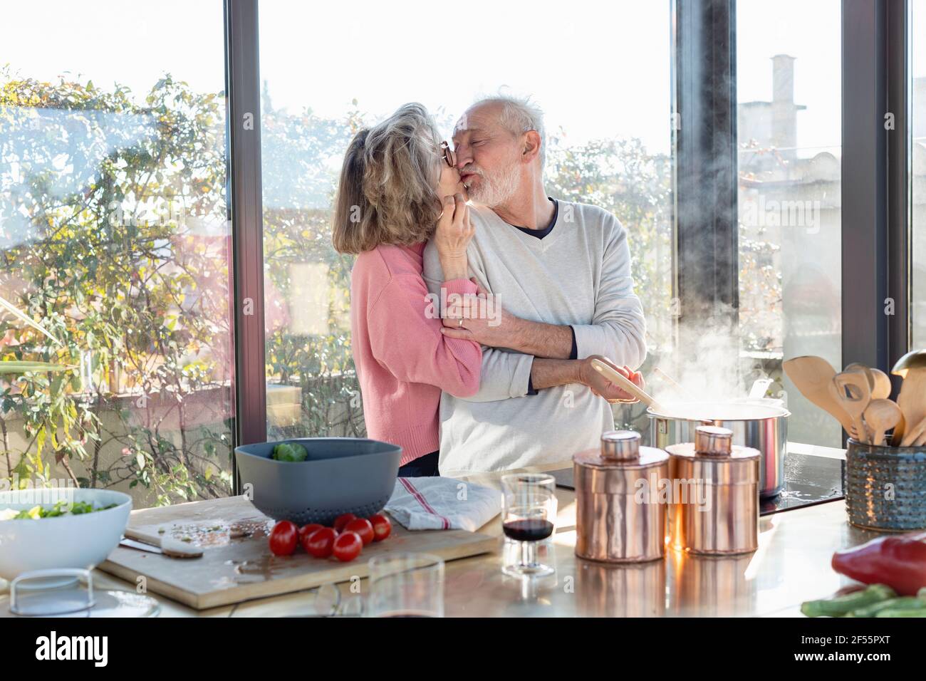 Senior couple kissing each other while standing by kitchen island at home Stock Photo