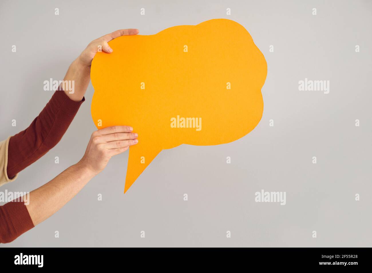 Anonymous person holding amber orange copy space speech bubble on gray background Stock Photo