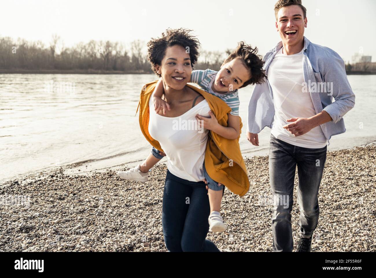Young woman piggybacking boy while running by lakeshore Stock Photo