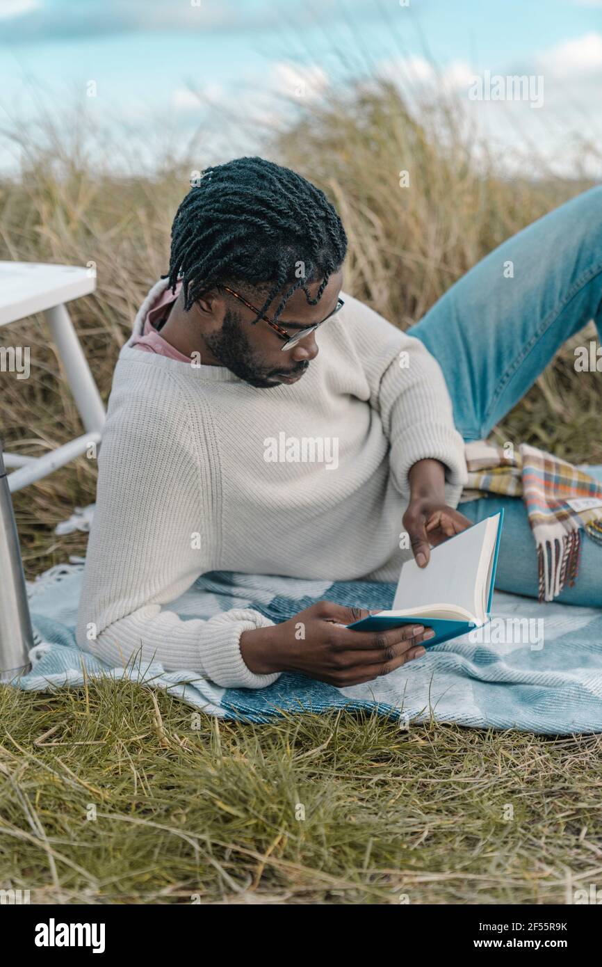Relaxed young man reading book while lying amidst dried plants Stock Photo