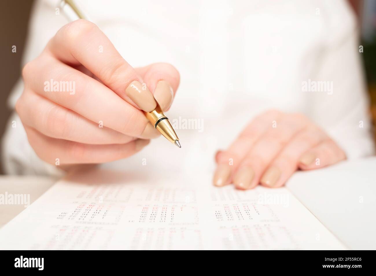 Female hand holding a pen to mark the date in calendar. Calendar reminder, daily planning Stock Photo