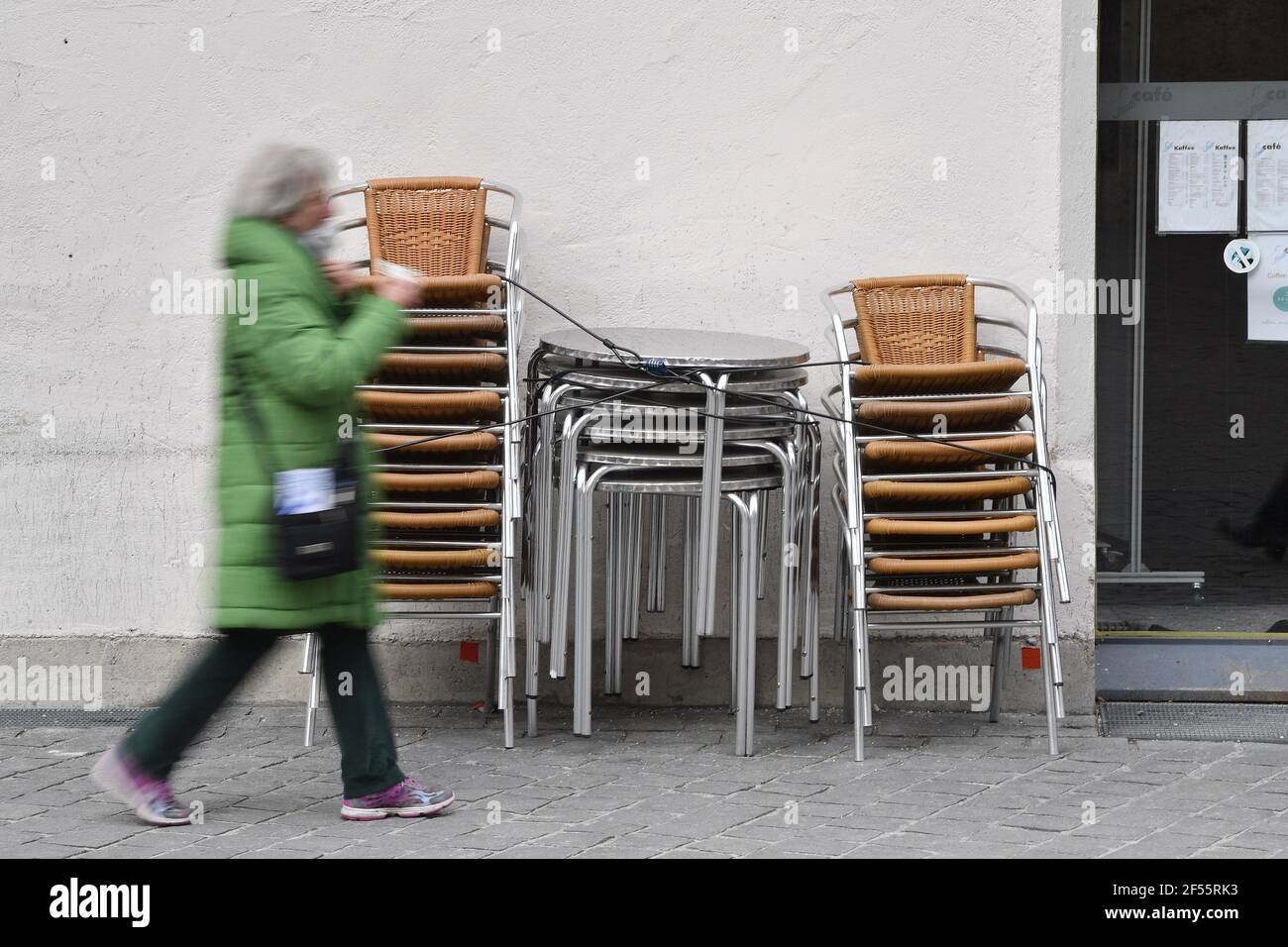 Munich, Deutschland. 23rd Mar, 2021. Topic picture: Coronavirus pandemic/consequences for gastronomy: A passer-by walks past stacked chairs and tables in front of a restaurant, cafe, outdoor catering on March 23, 2021. | usage worldwide Credit: dpa/Alamy Live News Stock Photo