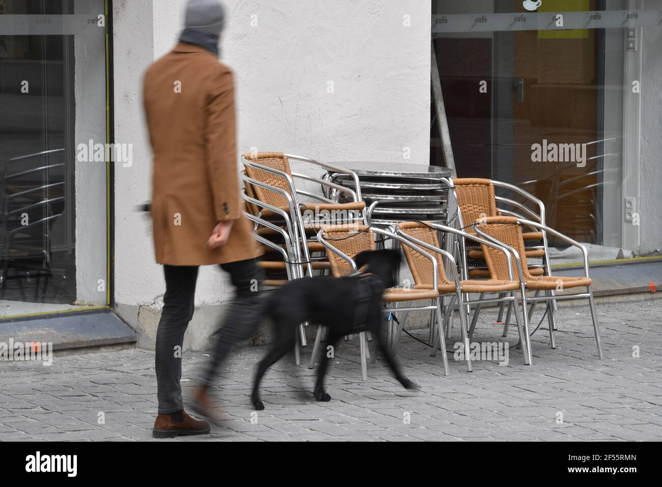 Munich, Deutschland. 23rd Mar, 2021. Topic picture: Coronavirus pandemic/consequences for gastronomy: A passerby walks with his dog past stacked chairs and tables in front of a restaurant, cafe, outdoor catering on March 23, 2021. | usage worldwide Credit: dpa/Alamy Live News Stock Photo