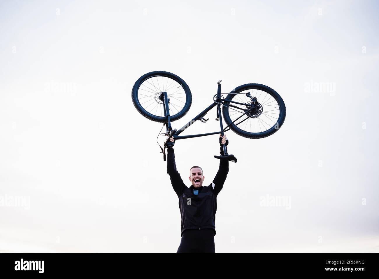 Cheerful sportsman lifting bicycle against sky Stock Photo