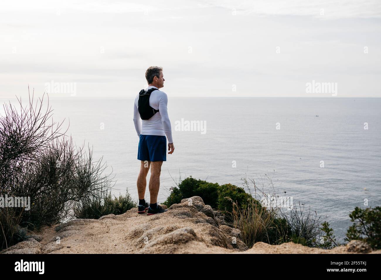 Mature man standing at mountain cliff near sea against clear sky Stock Photo