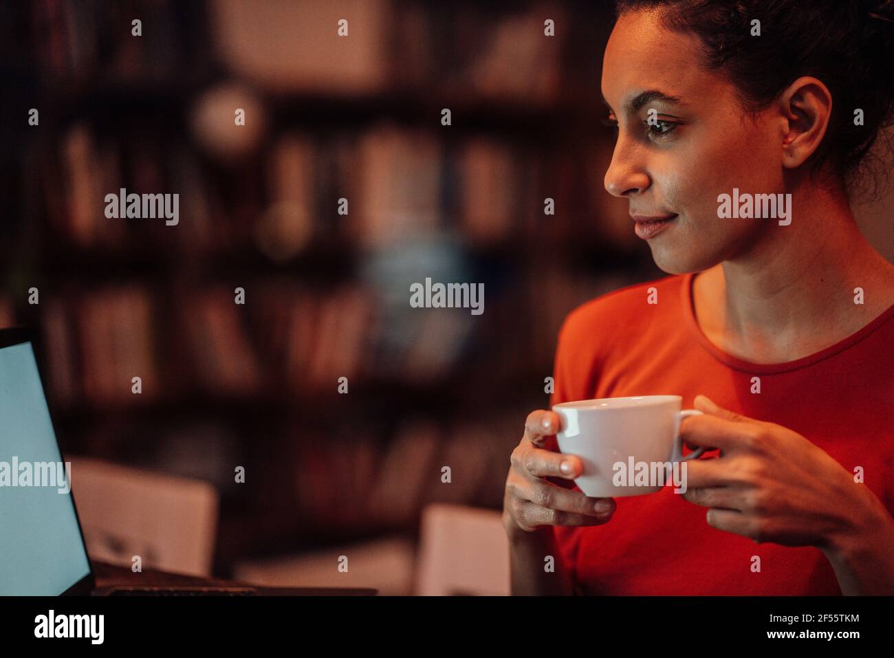 Smiling woman drinking coffee while using laptop sitting at cafe Stock Photo
