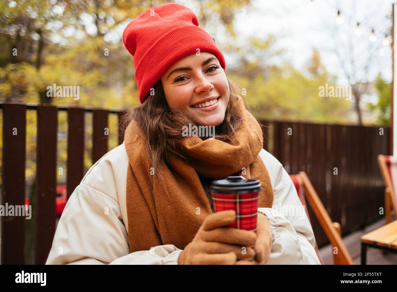 Woman with disposable coffee cup smiling while sitting at sidewalk cafe Stock Photo