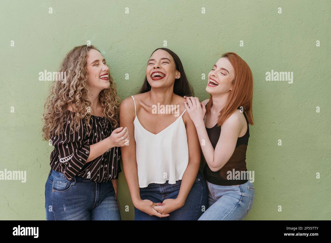 Multi ethnic female friends laughing against green wall Stock Photo