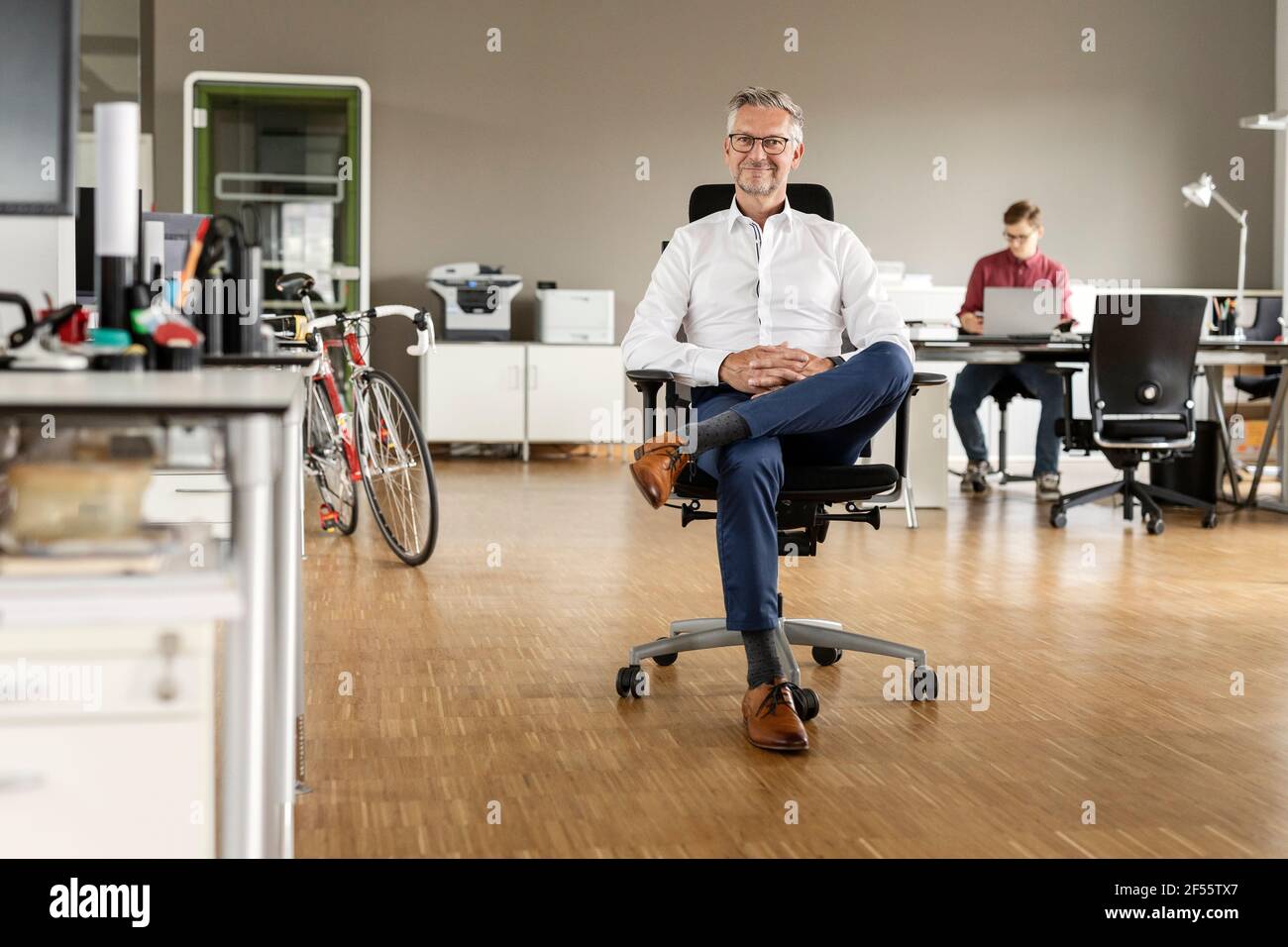 Smiling businessman with legs crossed at knee sitting on chair in office Stock Photo
