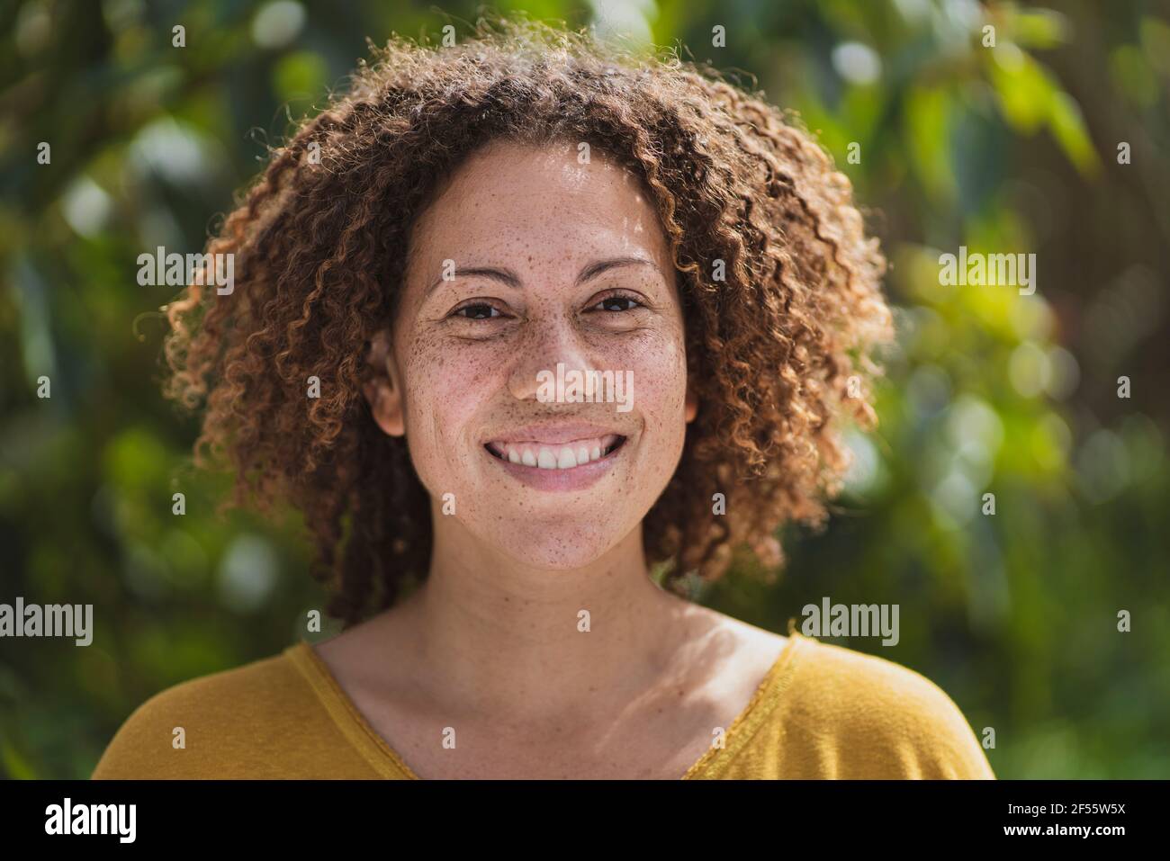 Smiling curly haired woman with freckles in vegetable garden Stock Photo