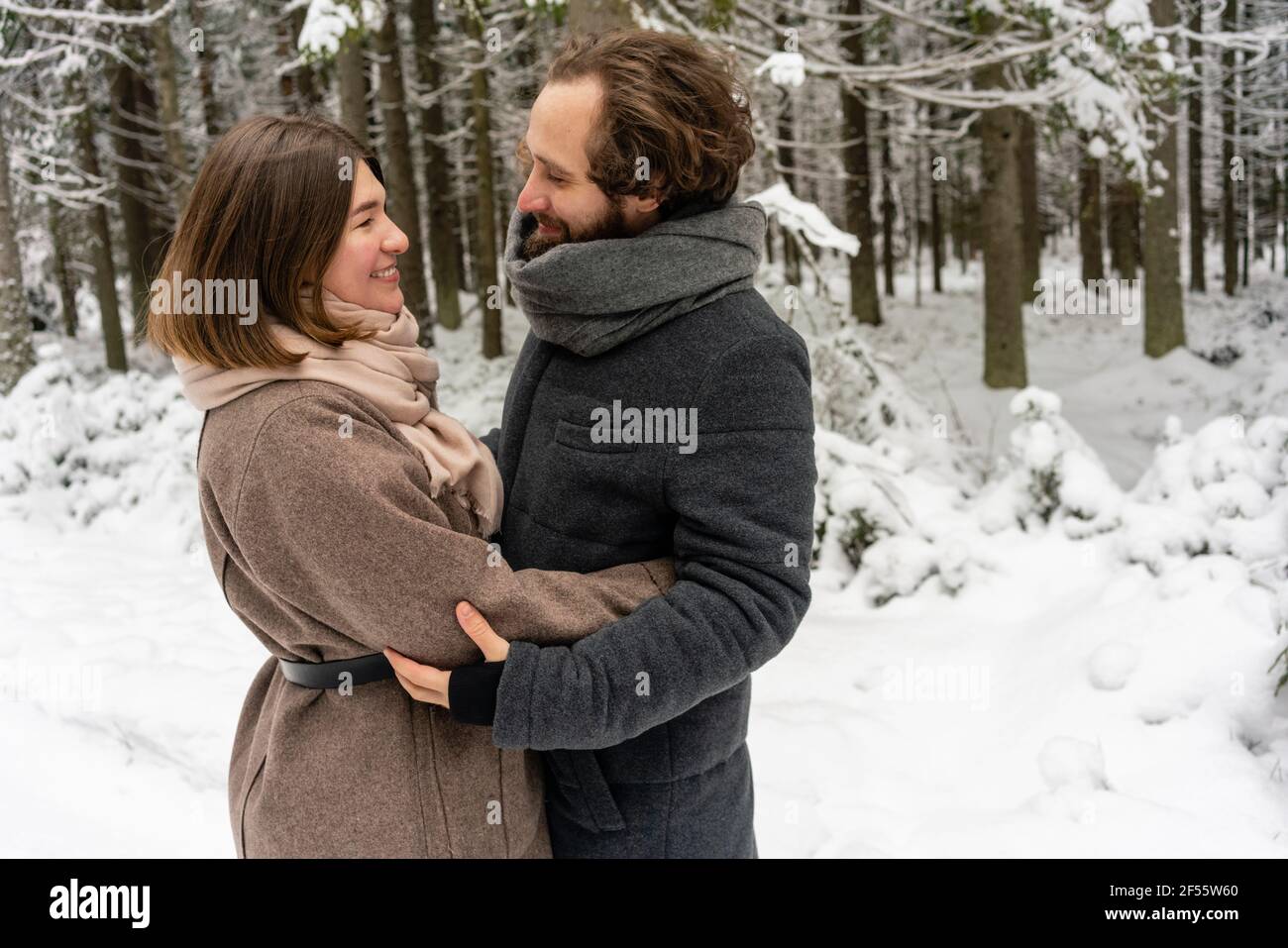Young couple smiling while standing together in forest Stock Photo