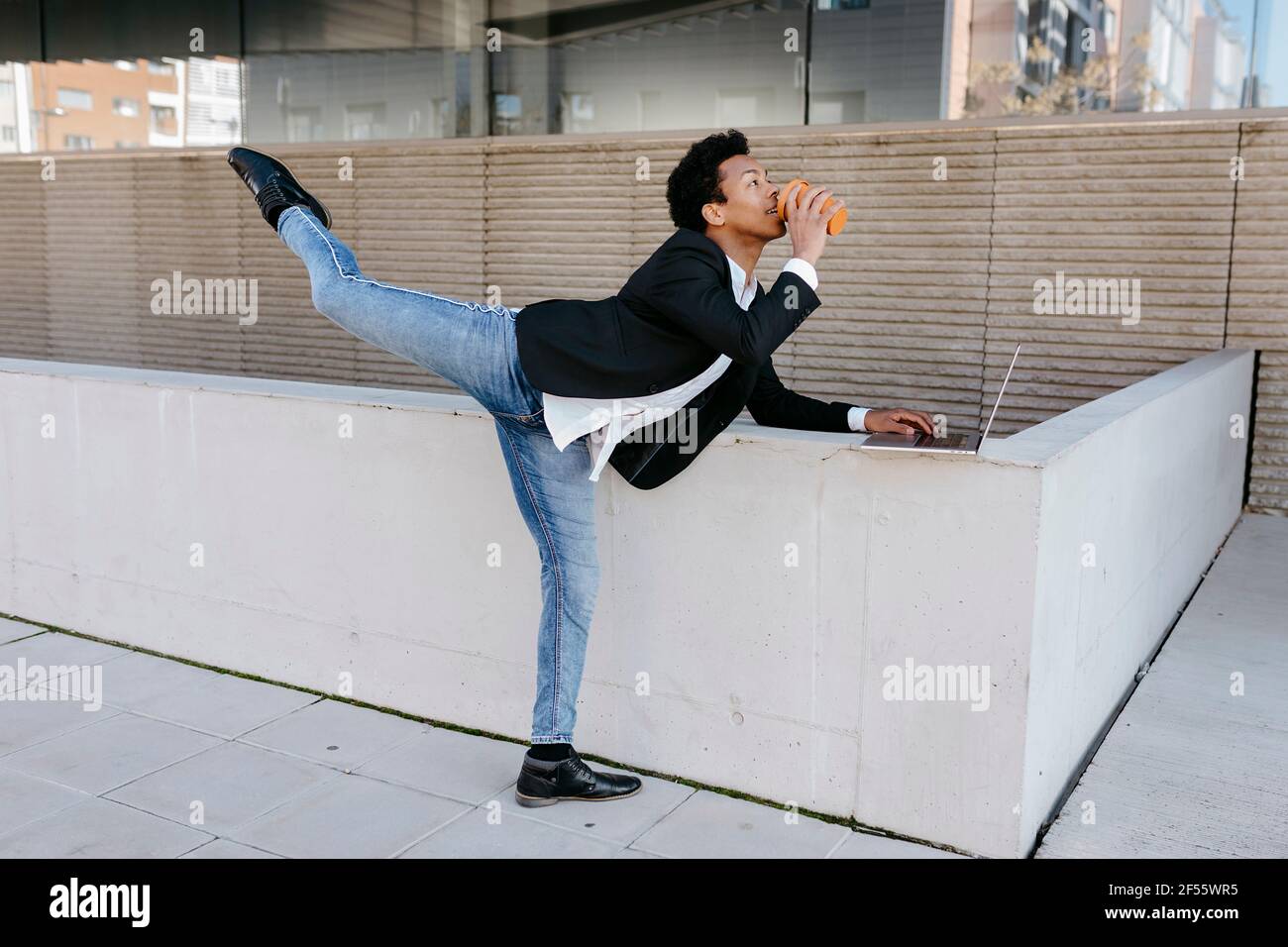 Flexible businessman with laptop drinking coffee while stretching leg Stock Photo