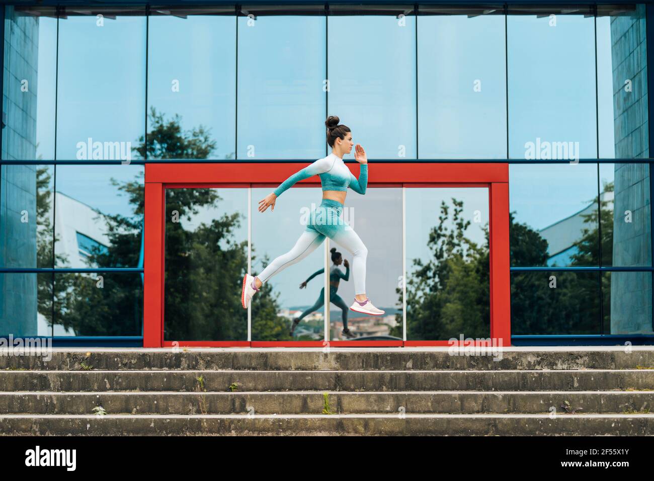 Active sportswoman running on steps by glass wall Stock Photo