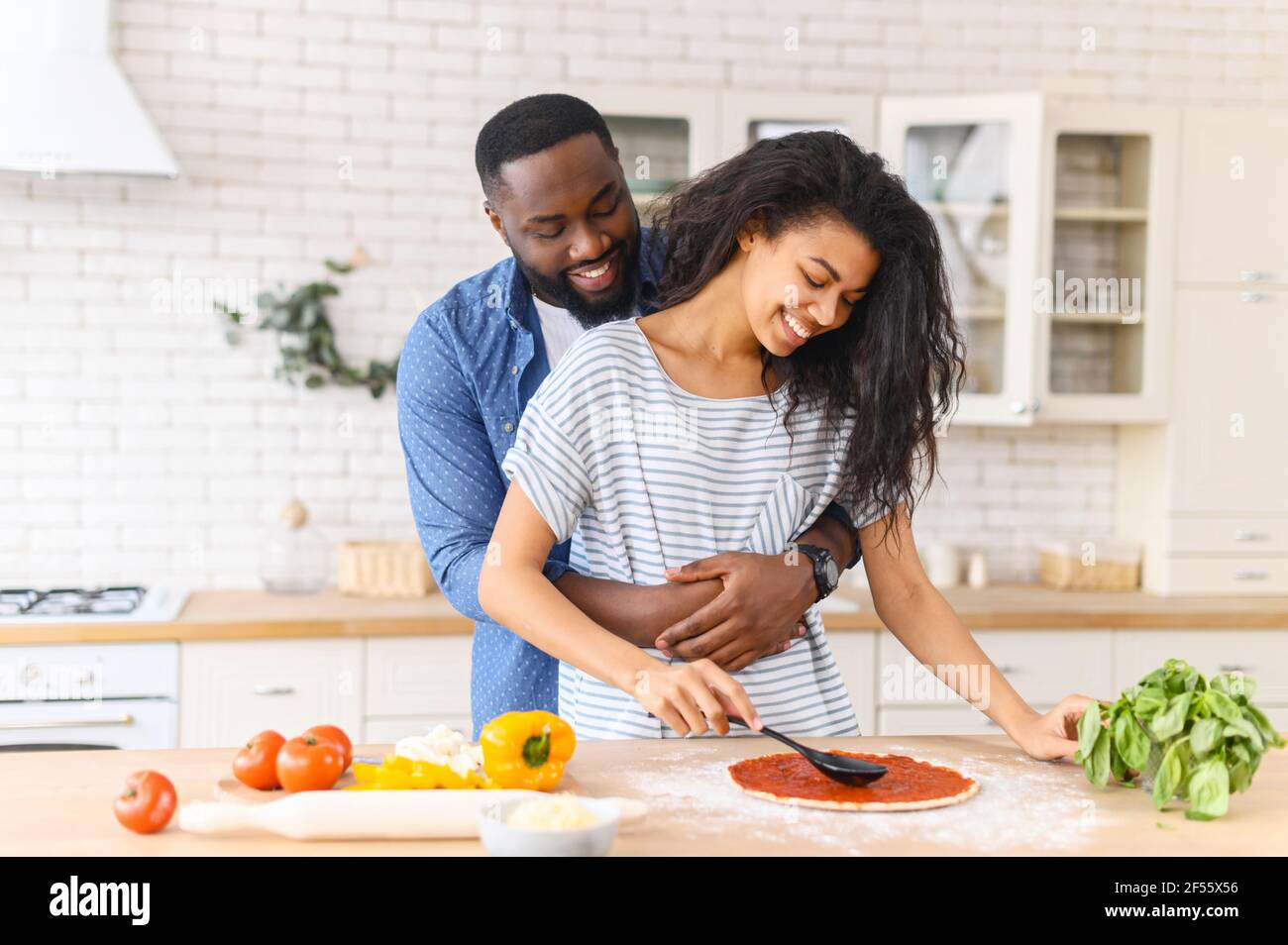 Loving young multiracial black couple making pizza together at kitchen  counter, young man hugging with love