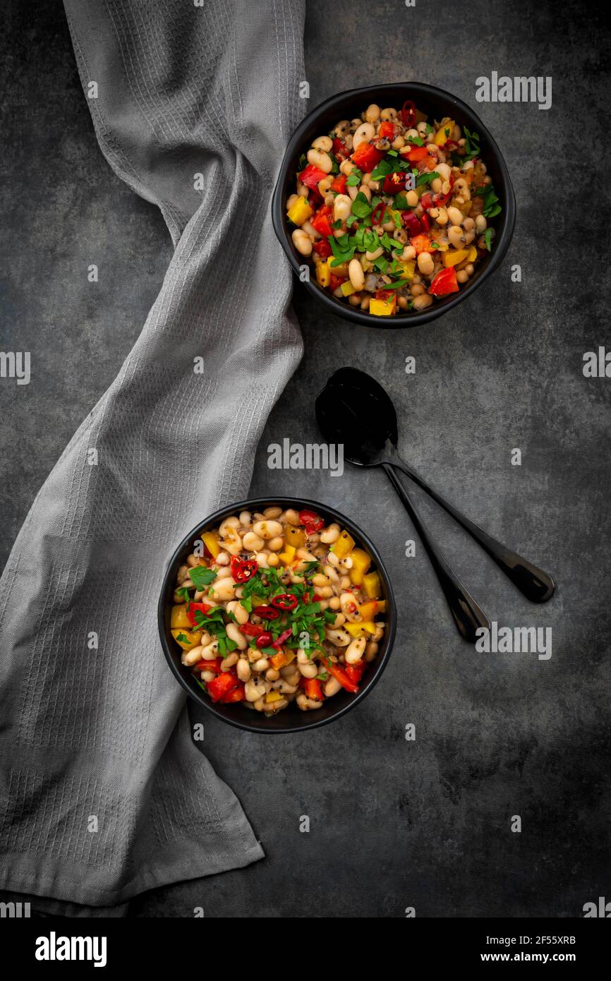 Studio shot of two bowls of bean stew with bell and chili peppers, quinoa and parsley Stock Photo