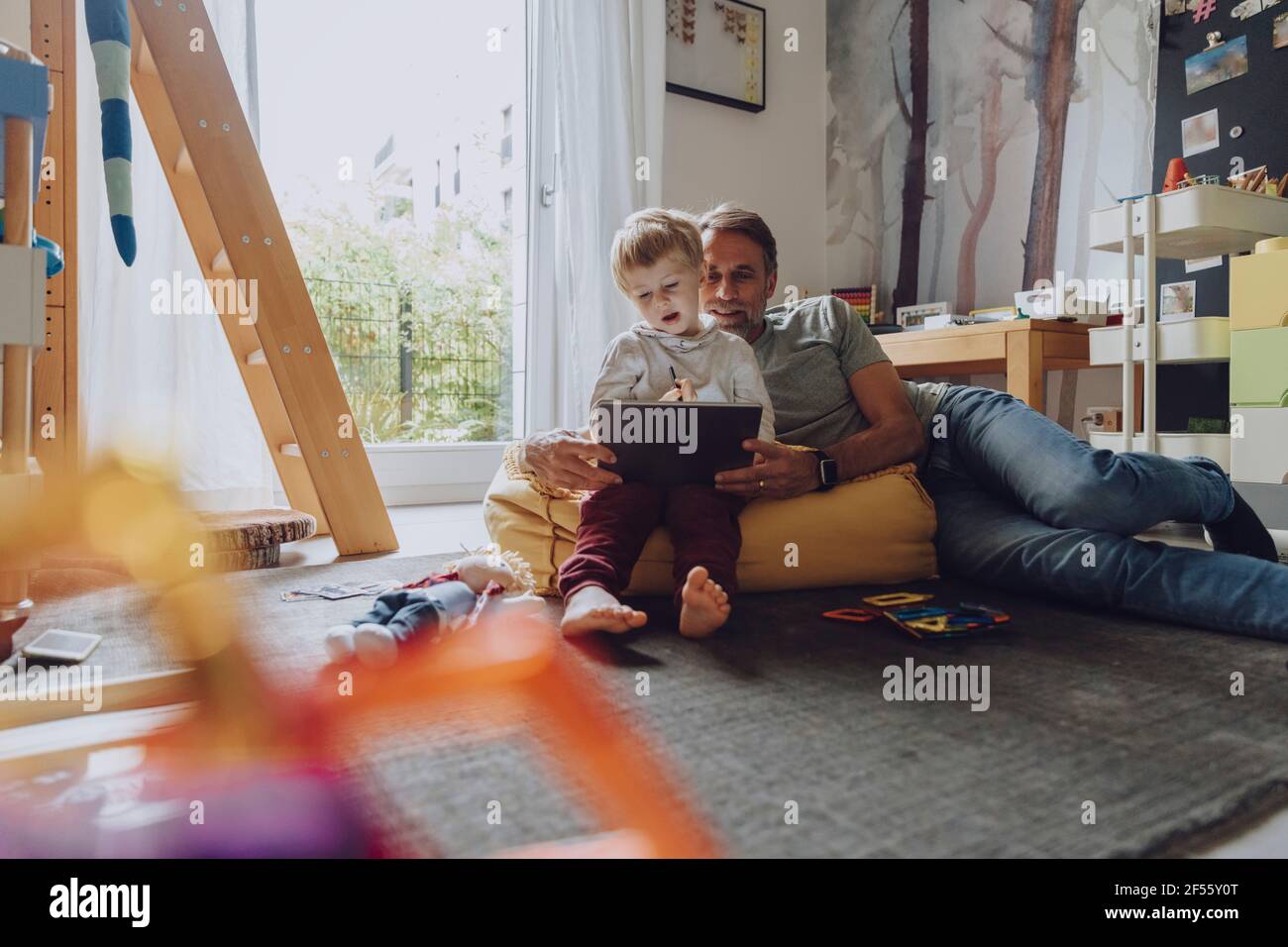 Father lying on bean bag while looking at son using tablet in bedroom Stock Photo