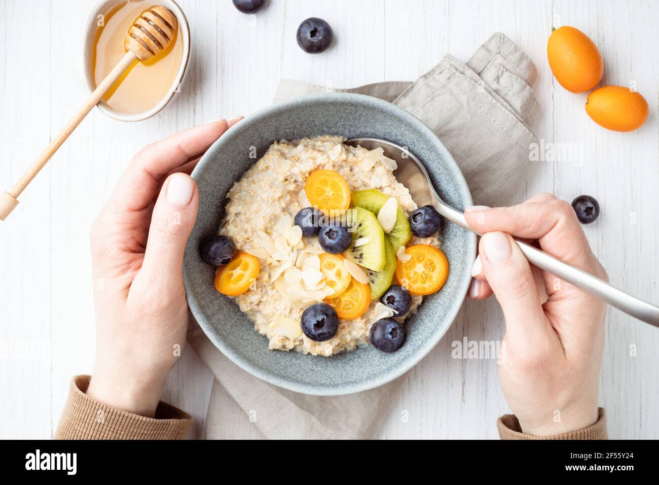 Female's hand scooping up an oatmeal porridge with blueberries and fruits. Healthy breakfast on a white table. Stock Photo