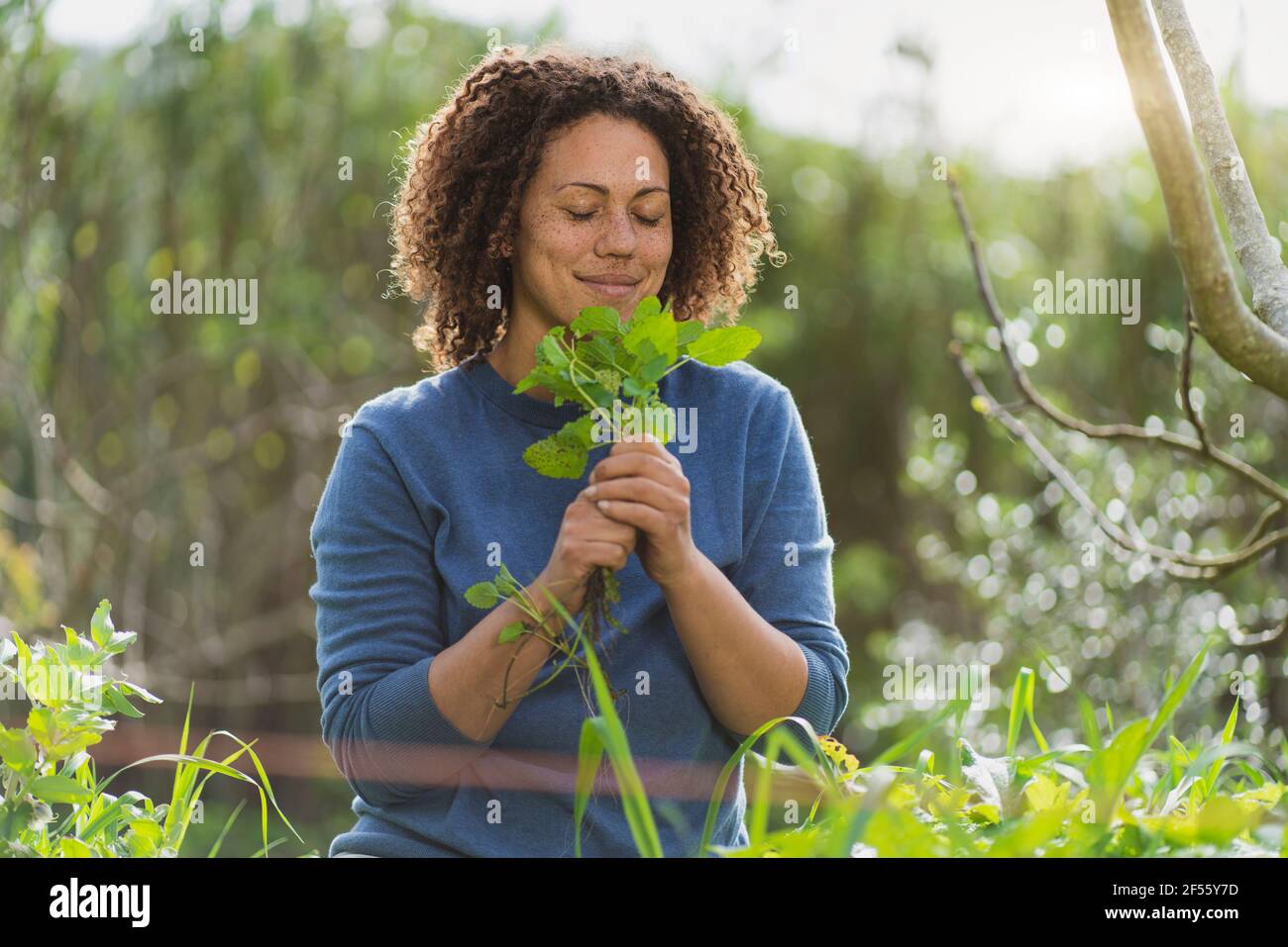 Woman with eyes closed smelling freshly picked organic mint in garden Stock Photo