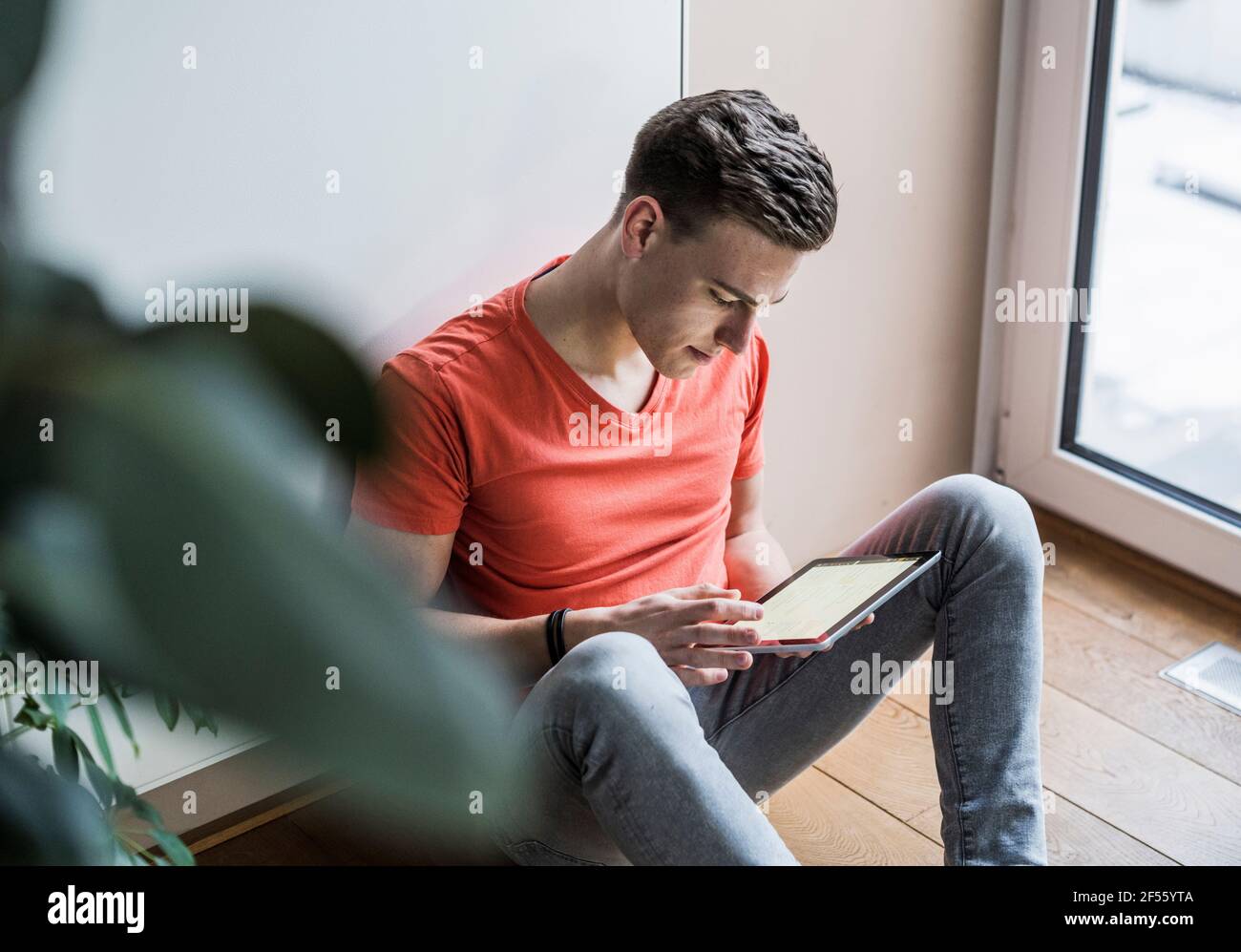 Young man using digital tablet while sitting against wall Stock Photo