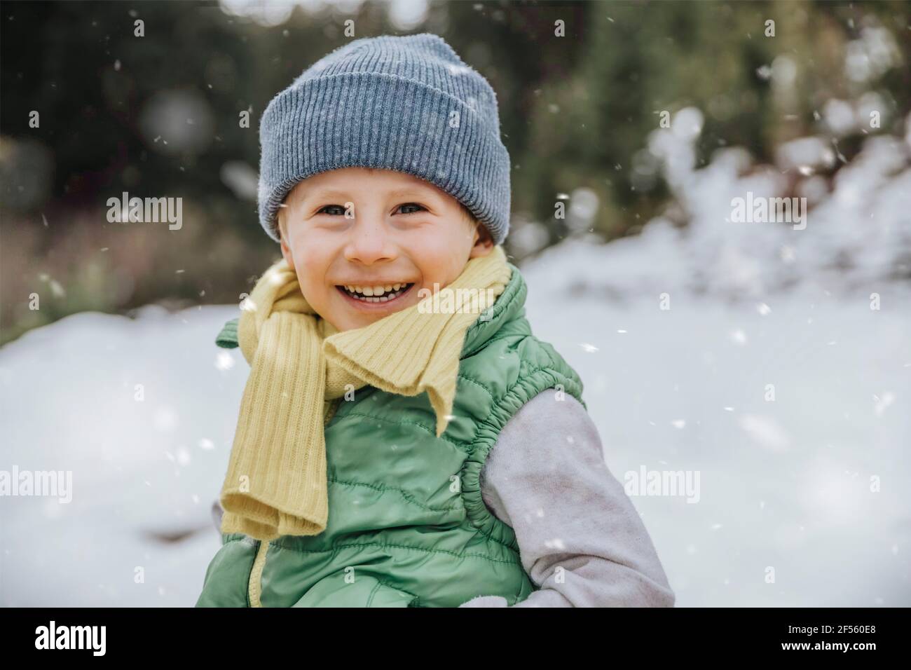Smiling cute boy on snow covered land while snowing during winter Stock Photo