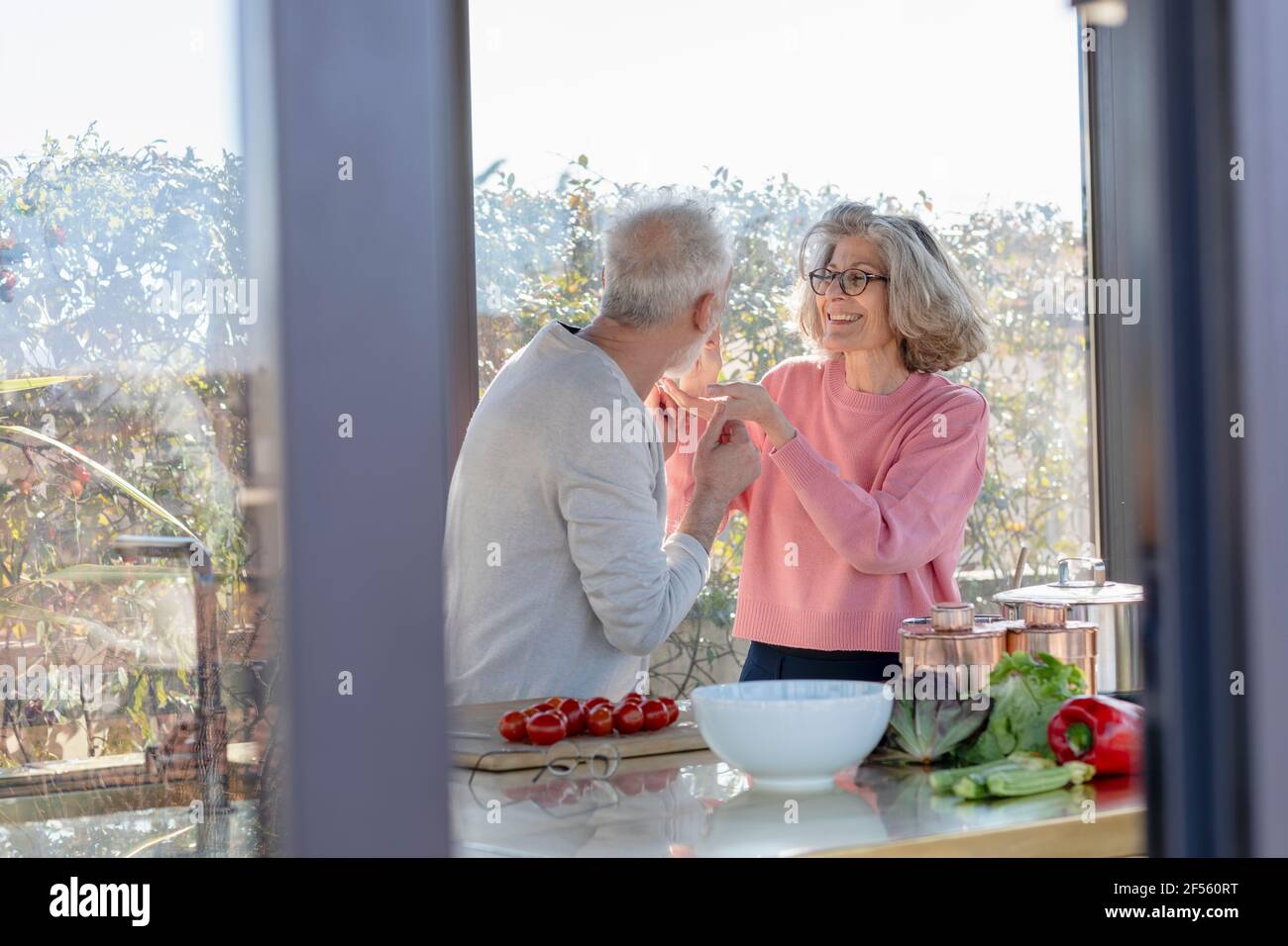 Senior woman feeding man while standing at home Stock Photo