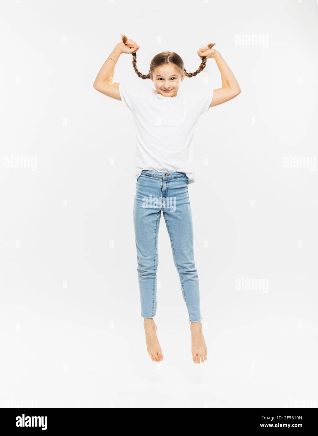 Girl holding her pigtail while jumping against white background Stock Photo