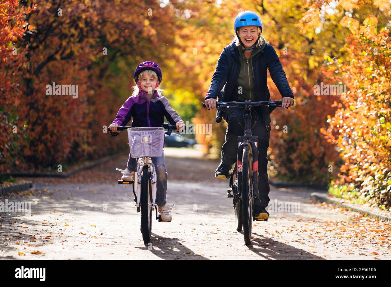 Happy mother and daughter cycling on road in park during autumn Stock Photo