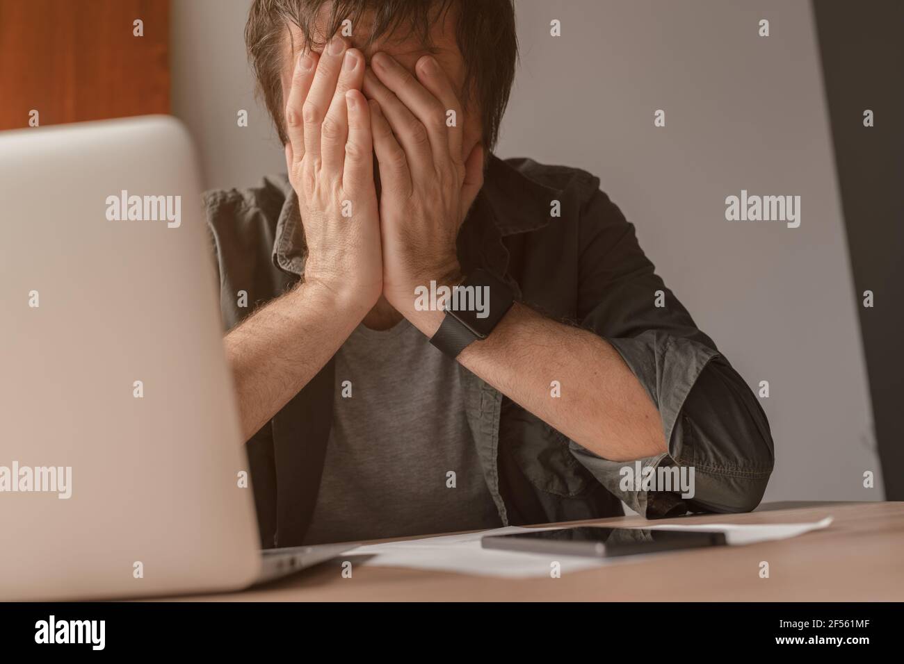 Disappointed freelancer with head in hands crying at home office desk Stock Photo