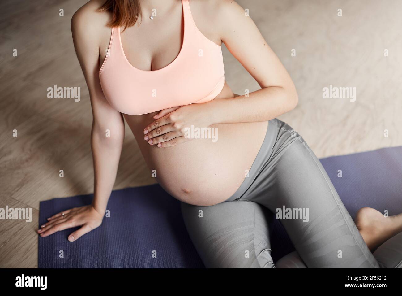 Vertical shot of cute happy european young pregnant woman in sports bra and  leggings, leaning on hand while lying on roll pad, touching belly, feeling  Stock Photo - Alamy