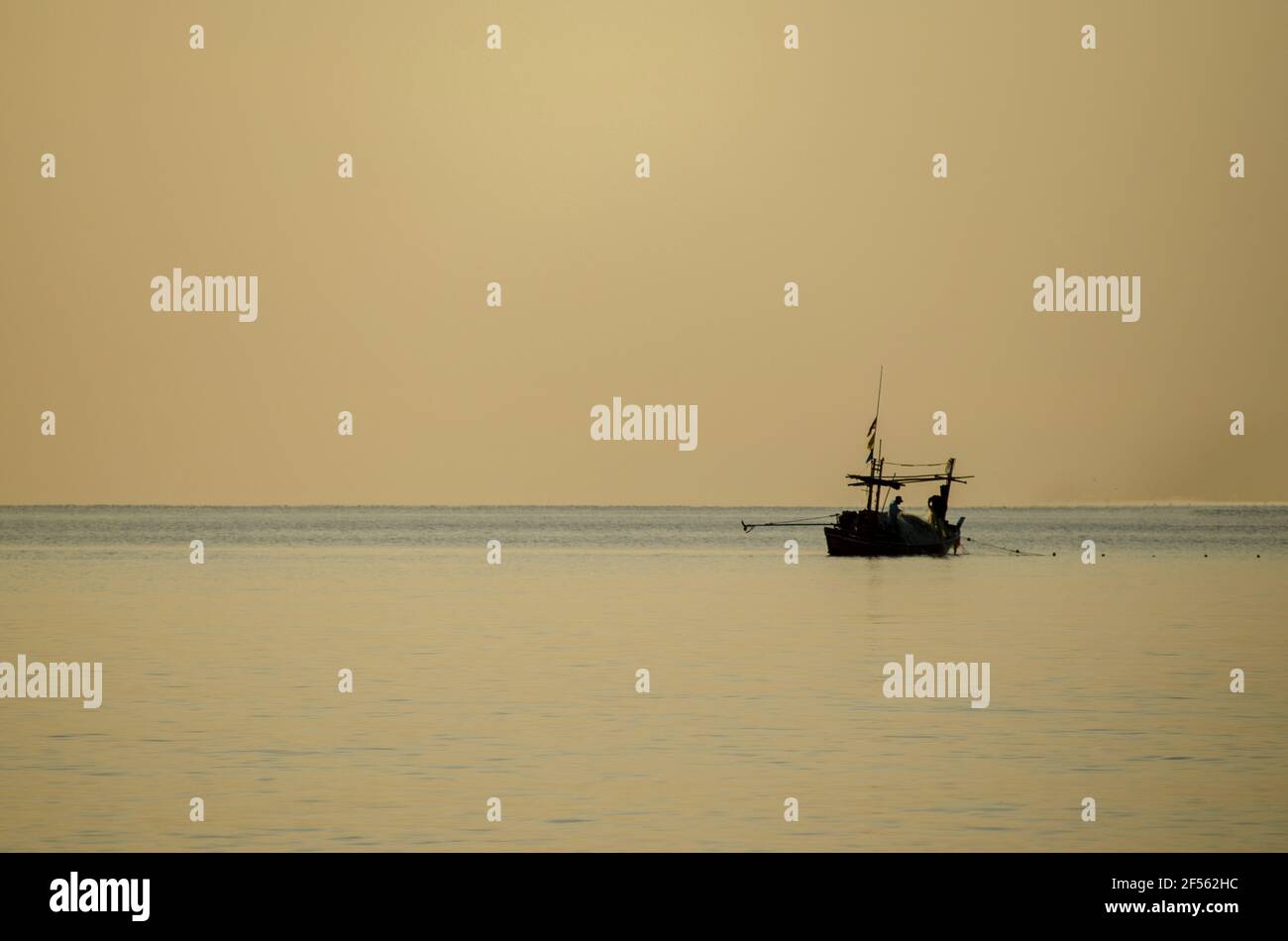Silhouette of fishermen collecting fishing gear on a small fishing boat ...