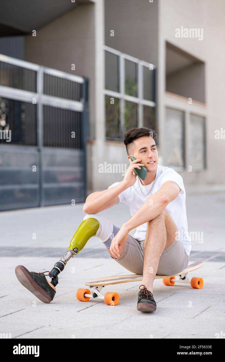 Young disabled man talking through mobile phone while sitting on skateboard Stock Photo