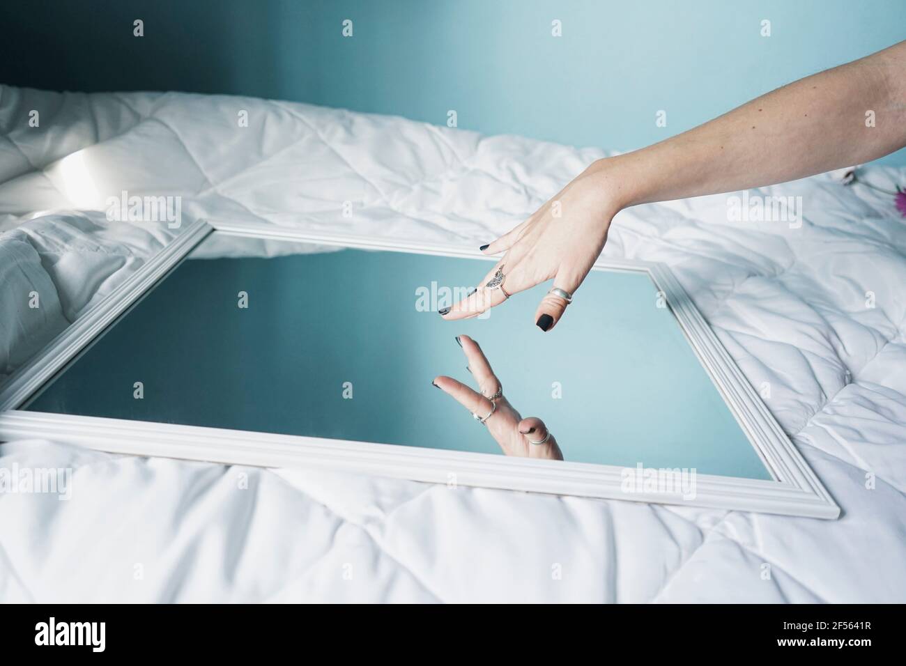 Hand of young woman ltouching mirror lying on white duvet Stock Photo