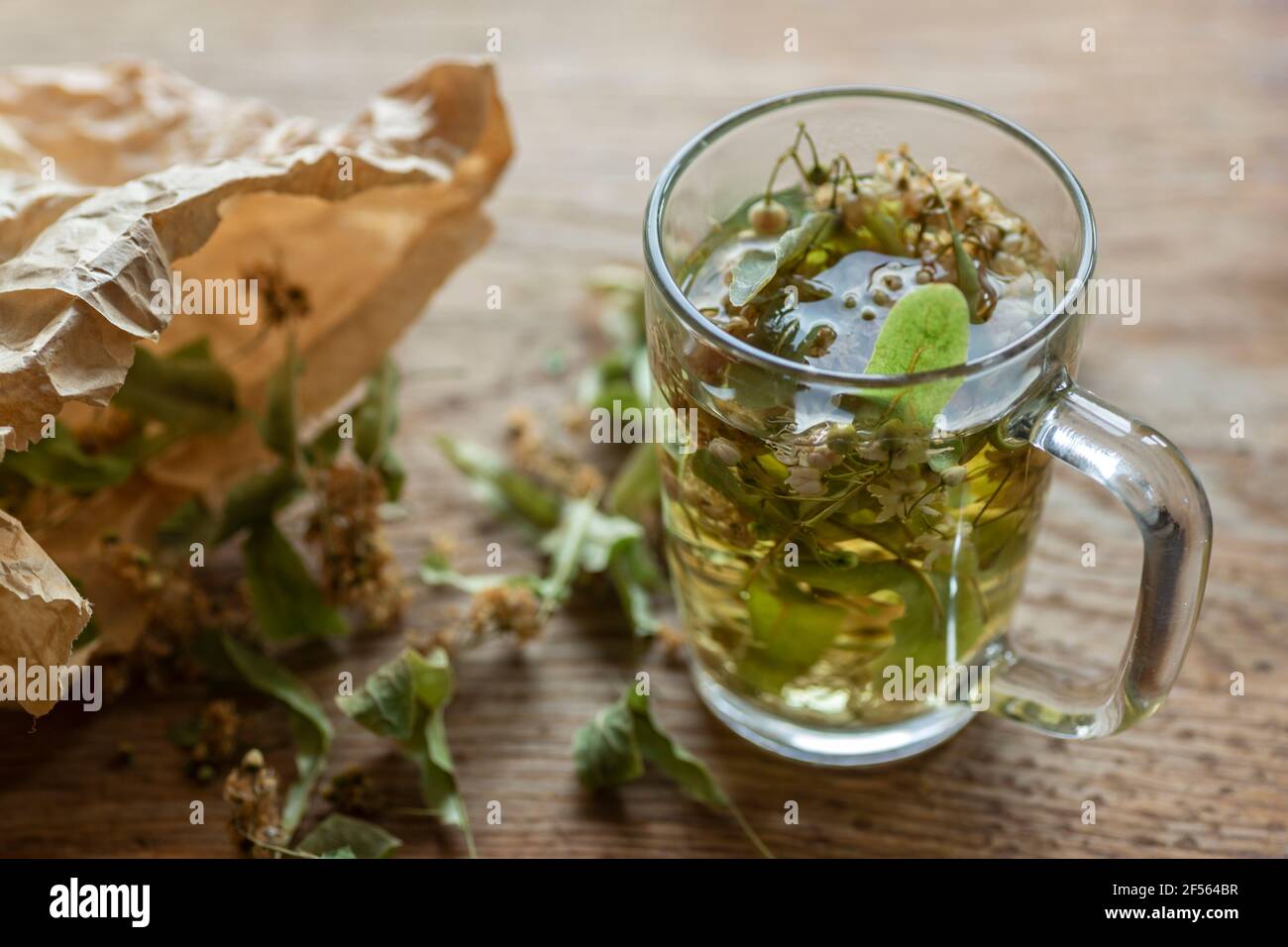Fresh lime tea by dried linden leaves in paper bag on wooden cutting board Stock Photo