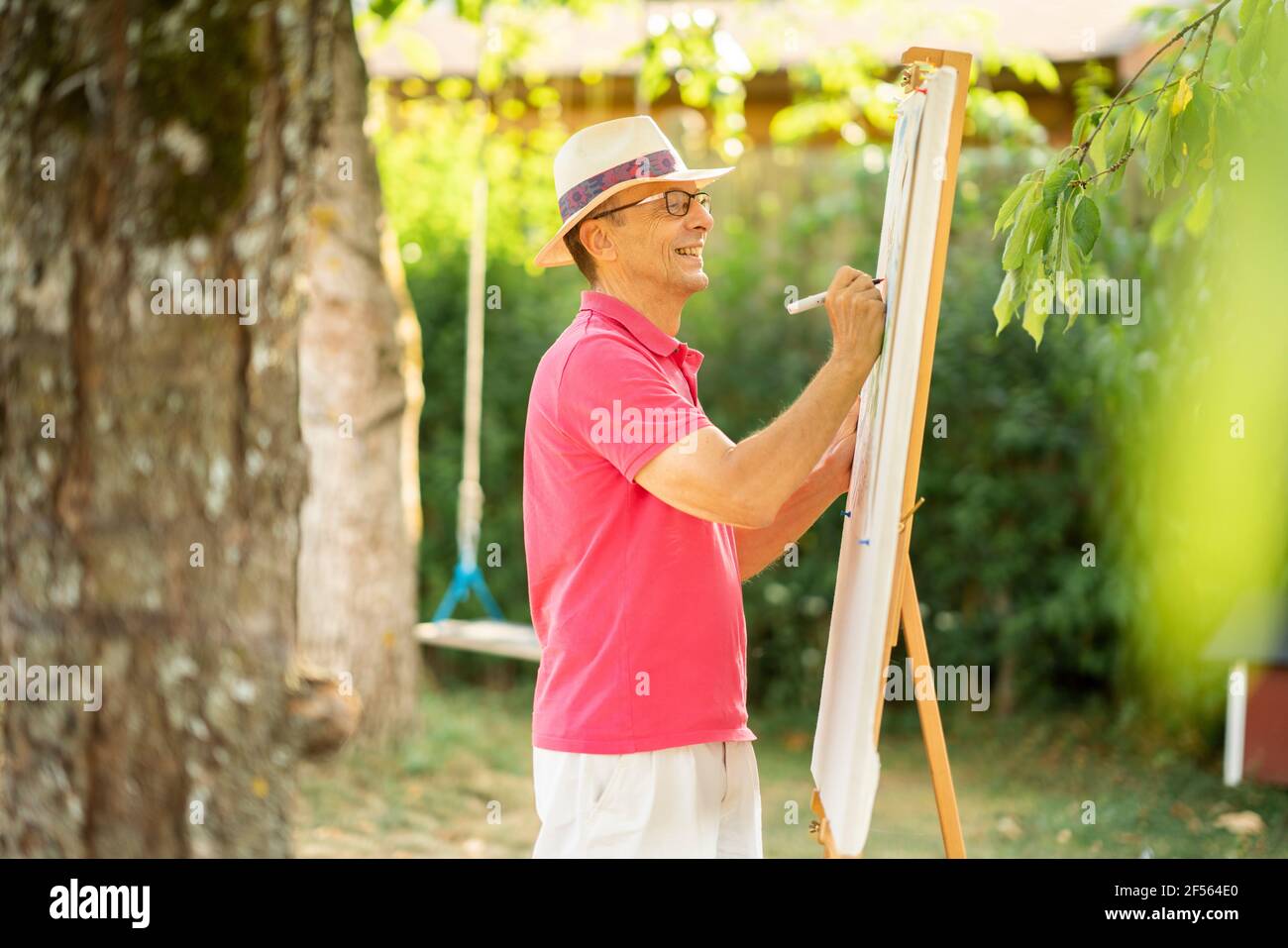 Happy elderly man drawing on canvas in garden Stock Photo