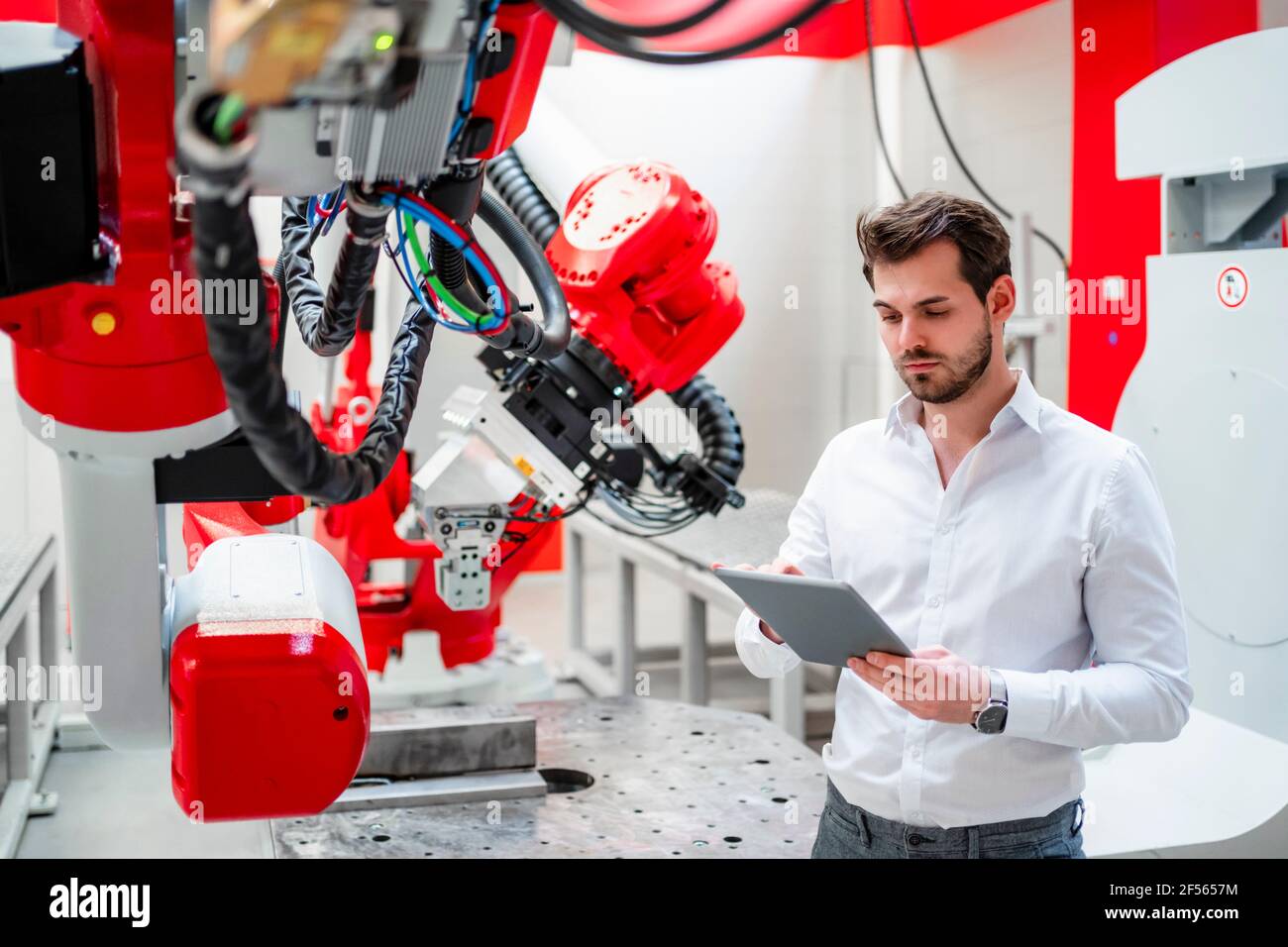 Young man using digital tablet by robotics in factory Stock Photo