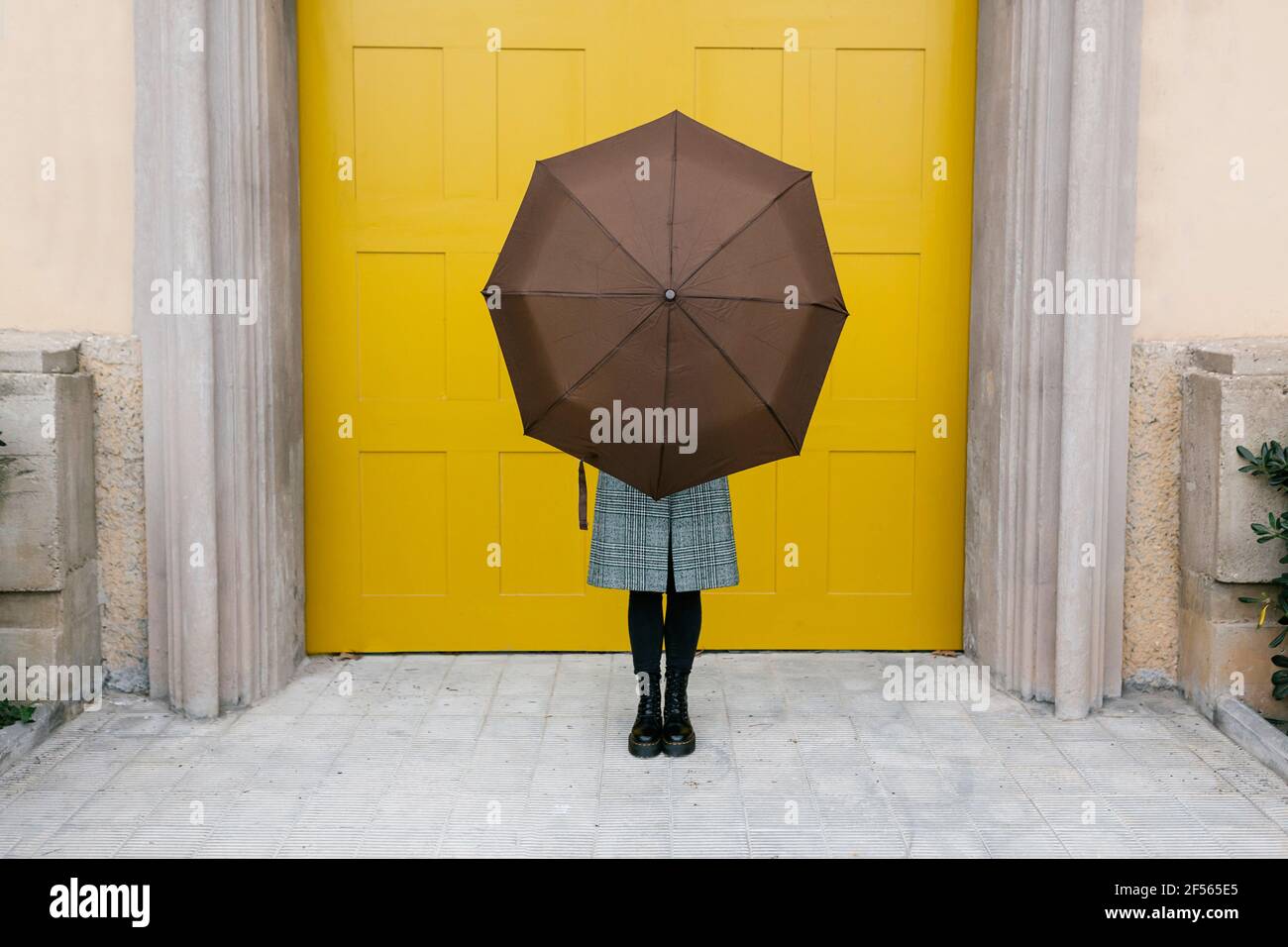 Woman holding umbrella while standing against yellow door Stock Photo
