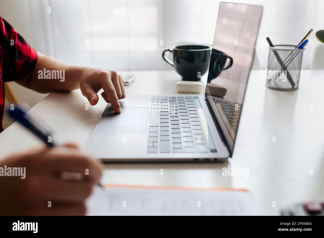 Man writing while using laptop on table at home office Stock Photo