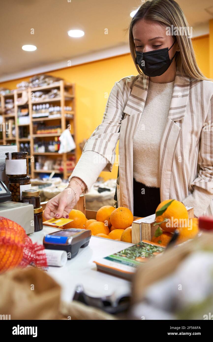 Young woman with protective face mask paying through credit card at store Stock Photo