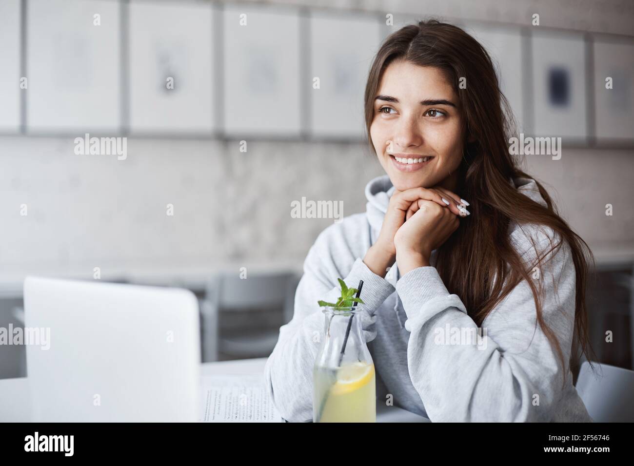 Young female student using a laptop between seminars to chat with her significant other. Drinking lemonade, smiling, dreaming of her holidays. Stock Photo