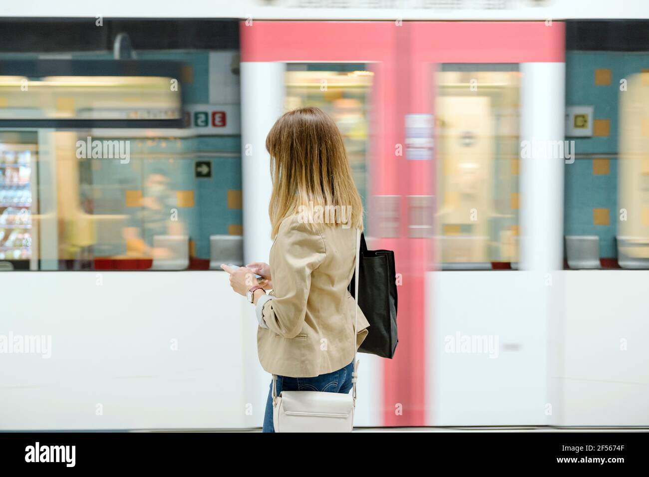 Woman in casual clothing using smart phone by subway train during COVID-19 Stock Photo
