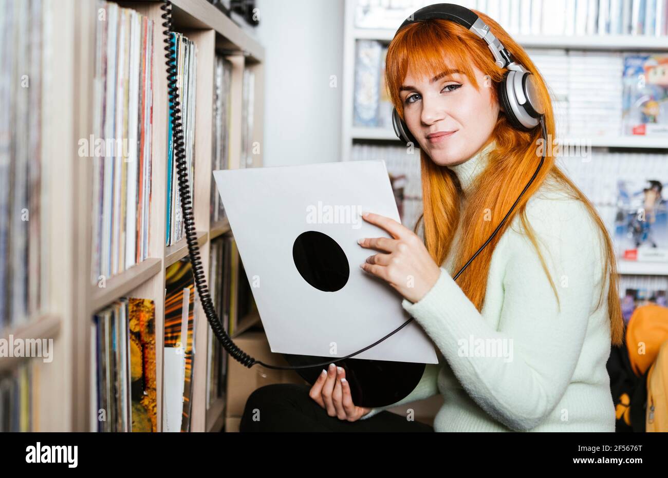 Smiling woman with headphones listening music while holding record at music store Stock Photo