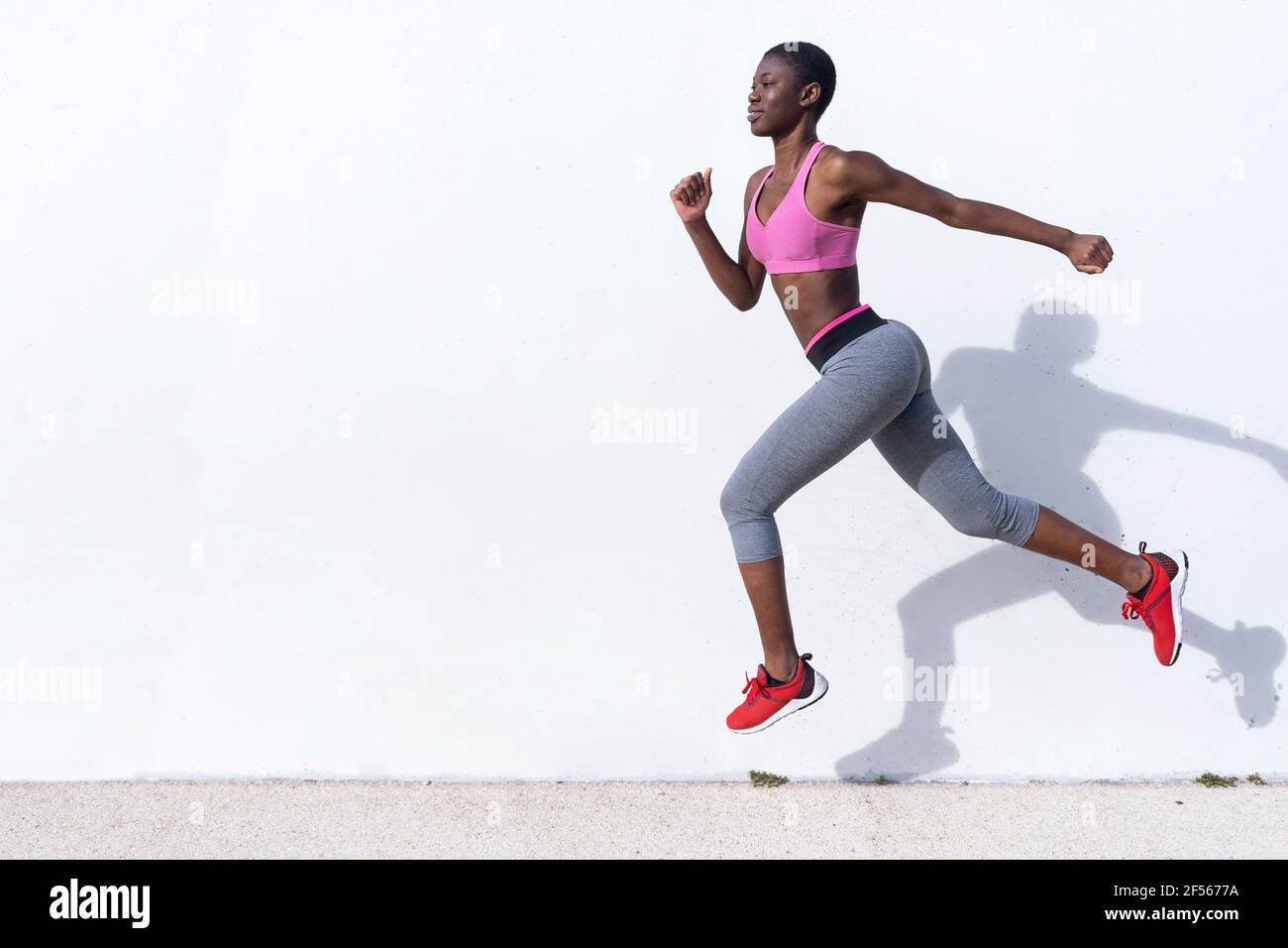 Young woman jumping against white wall during sunny day Stock Photo