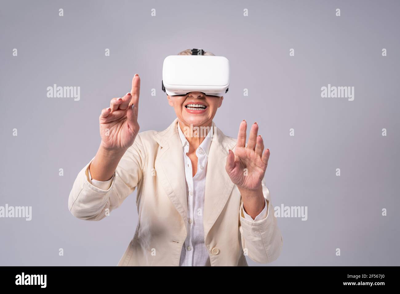 Senior businesswoman gesturing while using virtual reality headset while standing against gray background Stock Photo